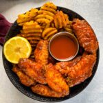 hot lemon pepper chicken wings in a black bowl with fresh lemon and hot sauce