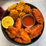 hot lemon pepper chicken wings in a black bowl with fresh lemon and hot sauce