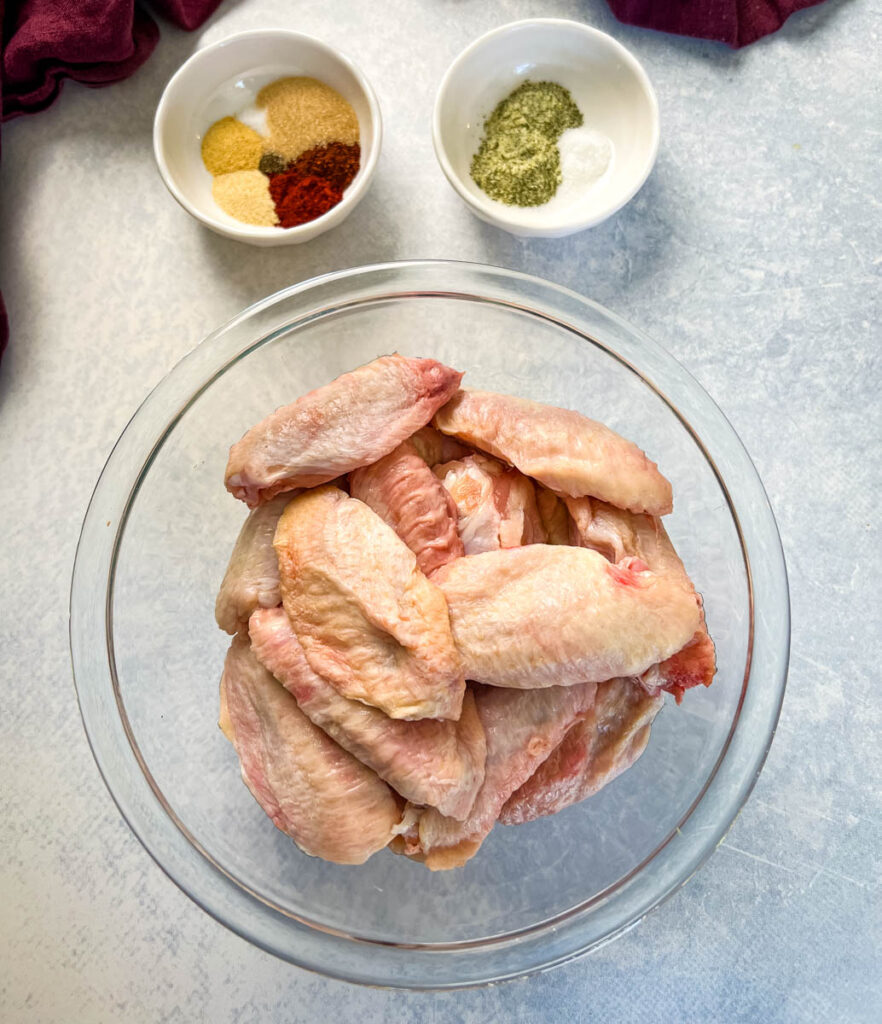 raw chicken wings in a bowl with 2 bowls of spices