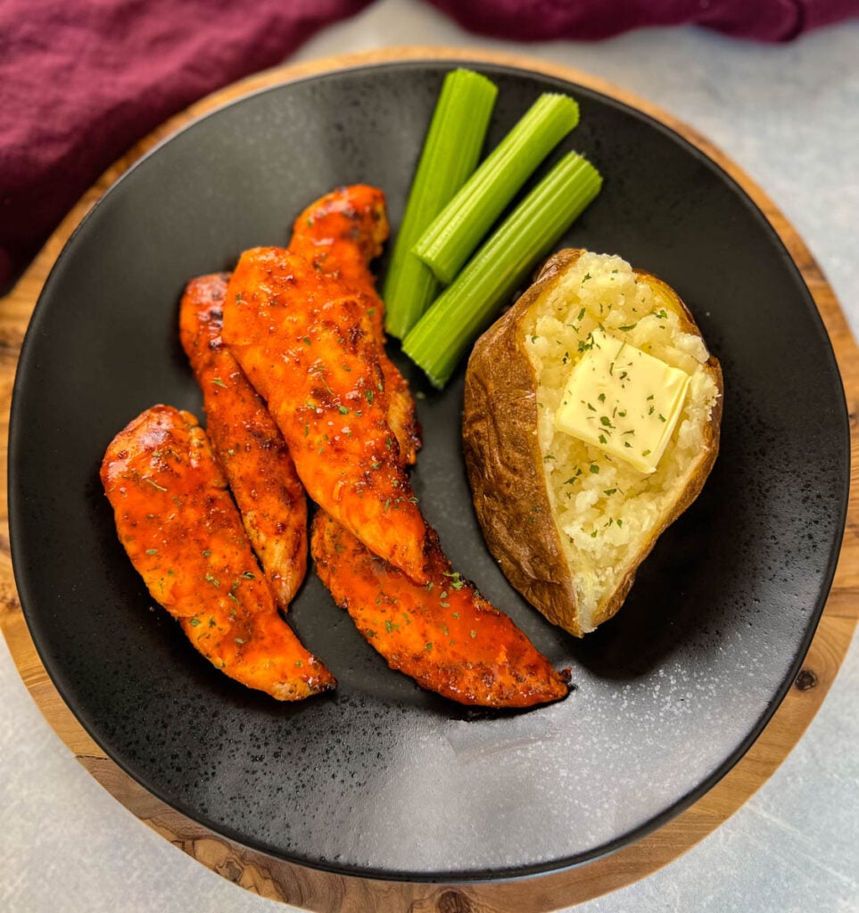 buffalo chicken tenders on a plate with celery, and a baked potato