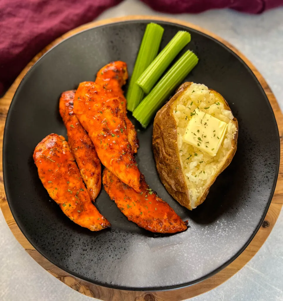 buffalo chicken tenders on a plate with celery, and a baked potato