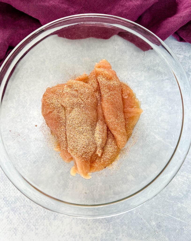 raw seasoned chicken tenderloins in a glass bowl