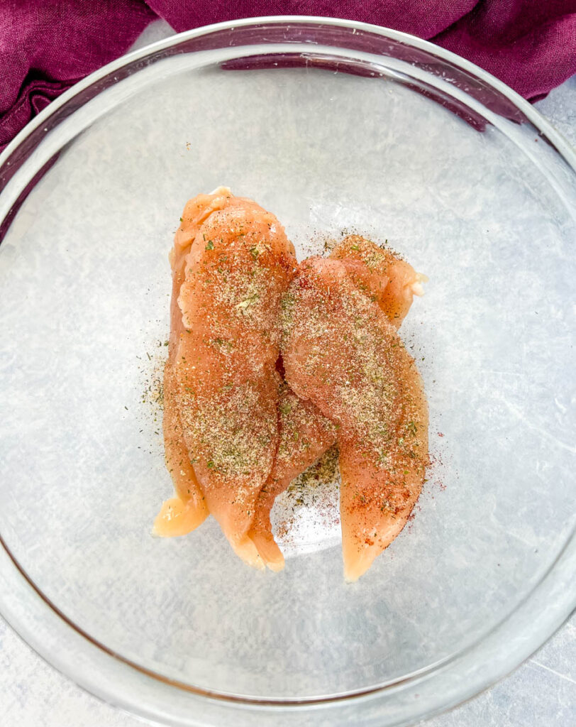 raw seasoned chicken tenderloins in a glass bowl