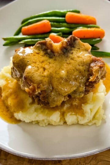 slow cooker crockpot oxtails with mashed potatoes, gravy, green beans, and carrots on a plate