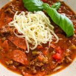 pizza soup with ground beef, pepperoni, mozzarella, and basil in a bowl