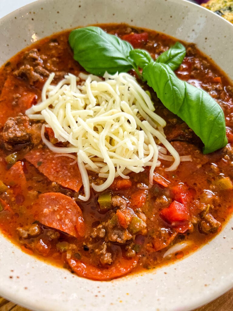 pizza soup with ground beef, pepperoni, mozzarella, and basil in a bowl