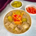 slow cooker cheeseburger soup in a white bowl with shredded cheese, pickles, and tomatoes