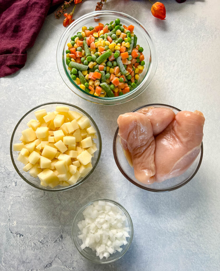 mixed vegetables, potatoes, raw chicken breasts, and chopped onions in separate glass bowls