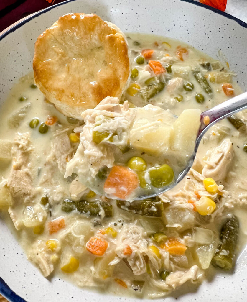a spoonful of chicken pot pie in a bowl with a biscuit