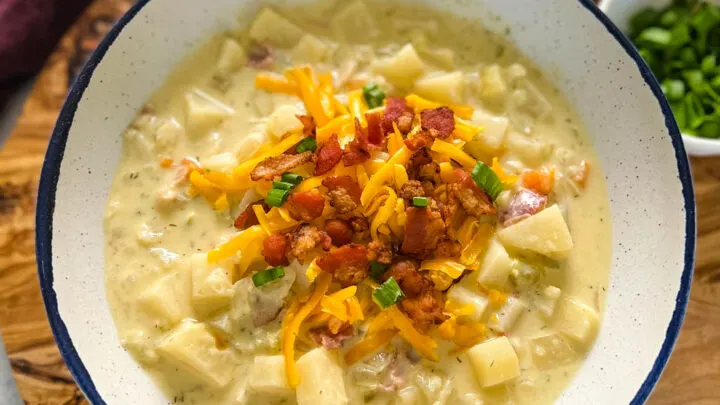 slow cooker loaded potato soup in a white bowl with bacon and cheese