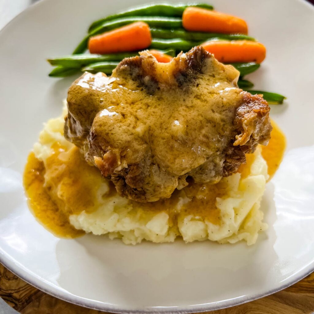 slow cooker crockpot oxtails with mashed potatoes, gravy, green beans, and carrots on a plate