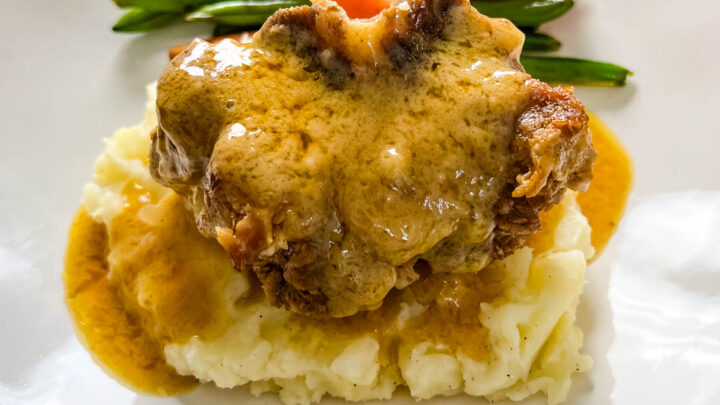 slow cooker crockpot oxtails with mashed potatoes, gravy, green beans, and carrots on a plate