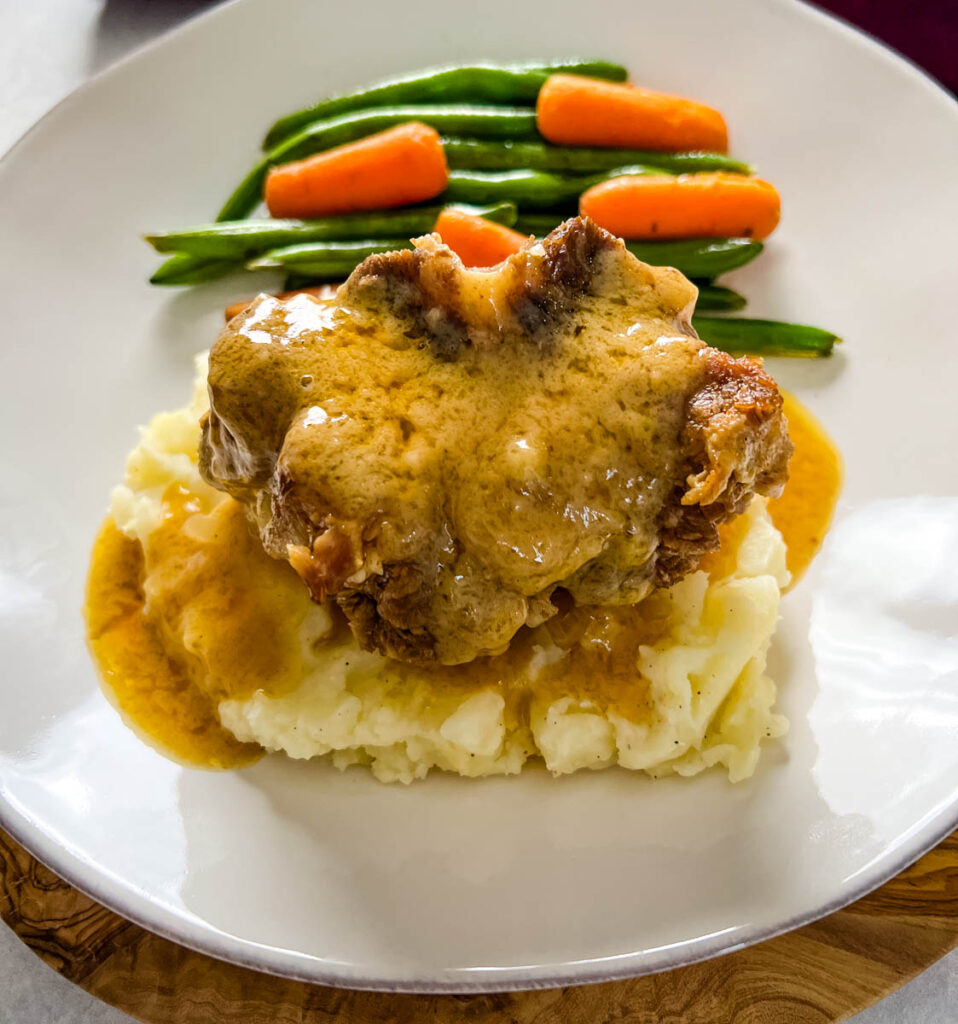 slow cooker crockpot oxtails with mashed potatoes, gravy, green beans, and carrots on a plate