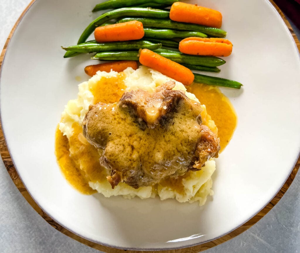 slow cooker crockpot oxtails with mashed potatoes, gravy, green beans, and carrots on a plate