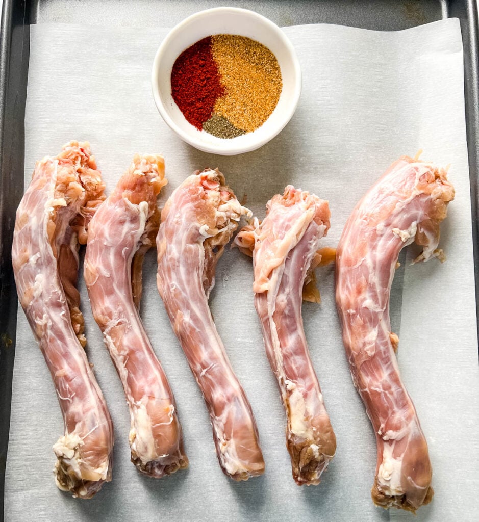 a bowl of spices and raw turkey necks on parchment paper