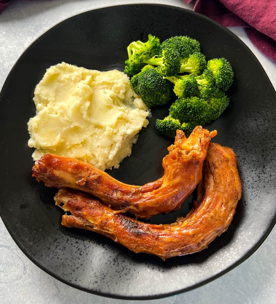 smoked turkey necks, mashed potatoes, and broccoli in a black plate