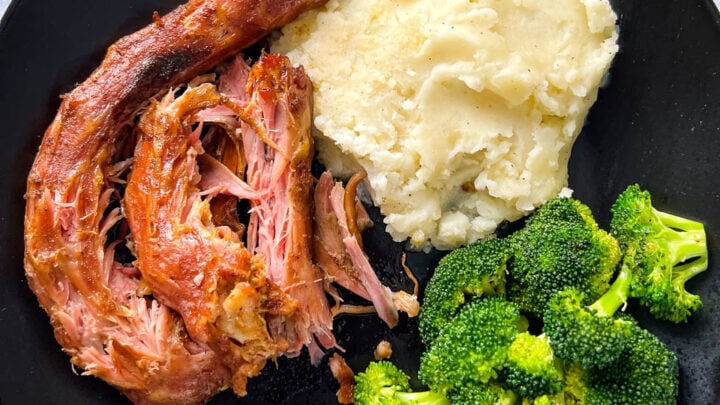 smoked turkey necks, mashed potatoes, and broccoli in a black plate