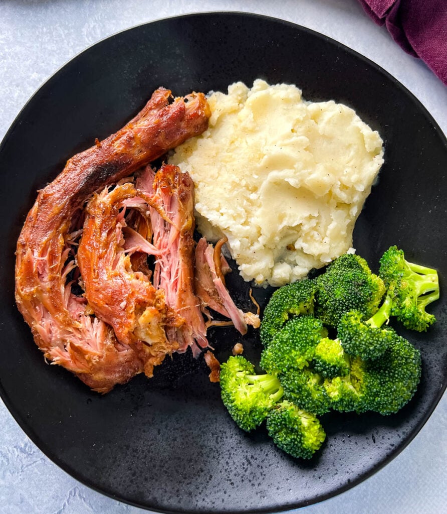smoked turkey necks, mashed potatoes, and broccoli in a black plate