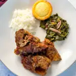 southern pork neck bones on a white plate with rice, collard greens, and cornbread