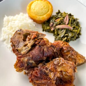 southern pork neck bones on a white plate with rice, collard greens, and cornbread