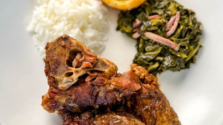 southern pork neck bones on a white plate with rice, collard greens, and cornbread
