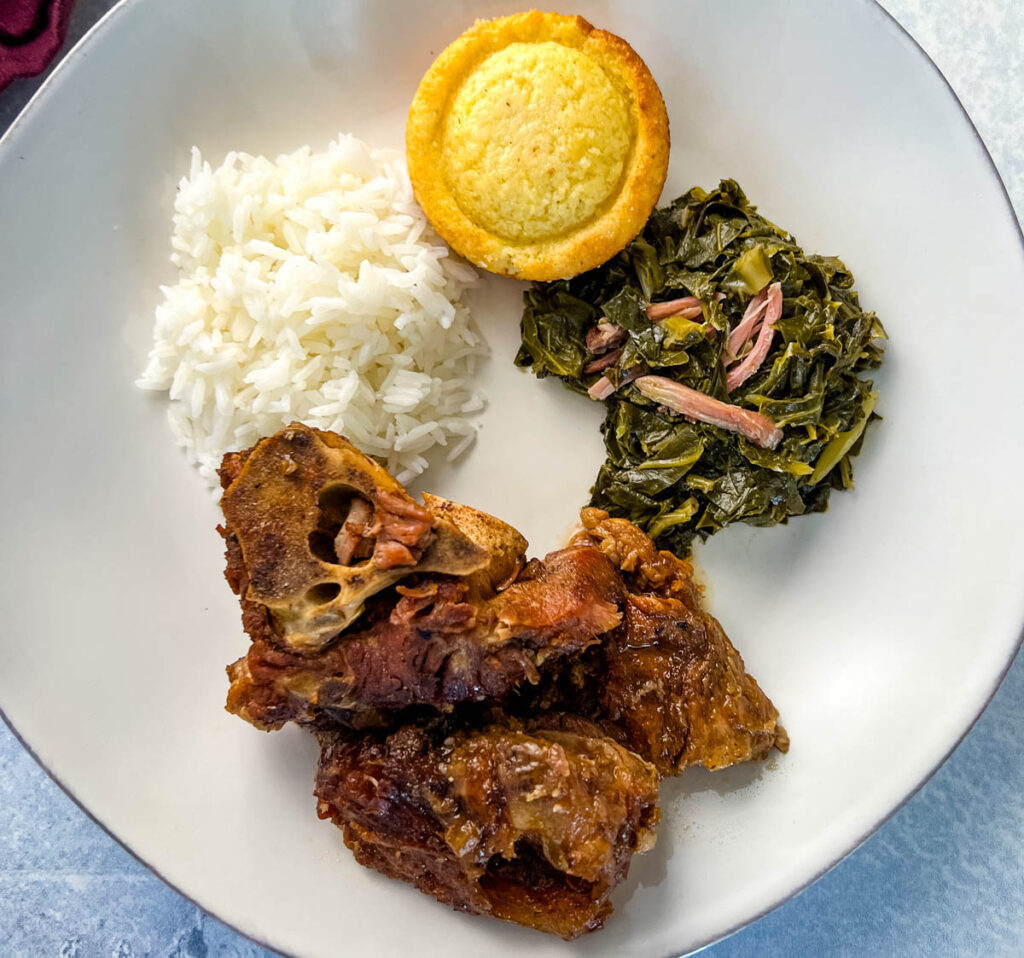 southern pork neck bones on a white plate with rice, collard greens, and cornbread