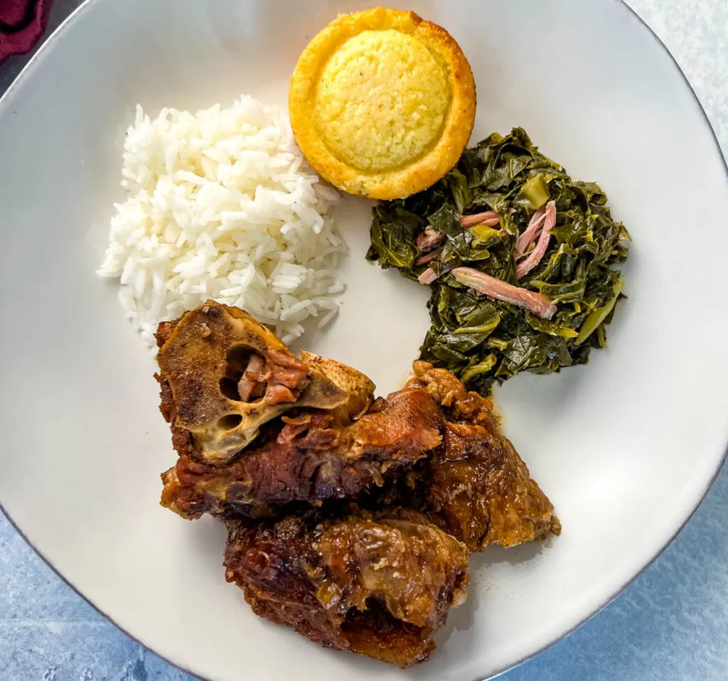 southern pork neck bones on a white plate with rice, collard greens, and cornbread