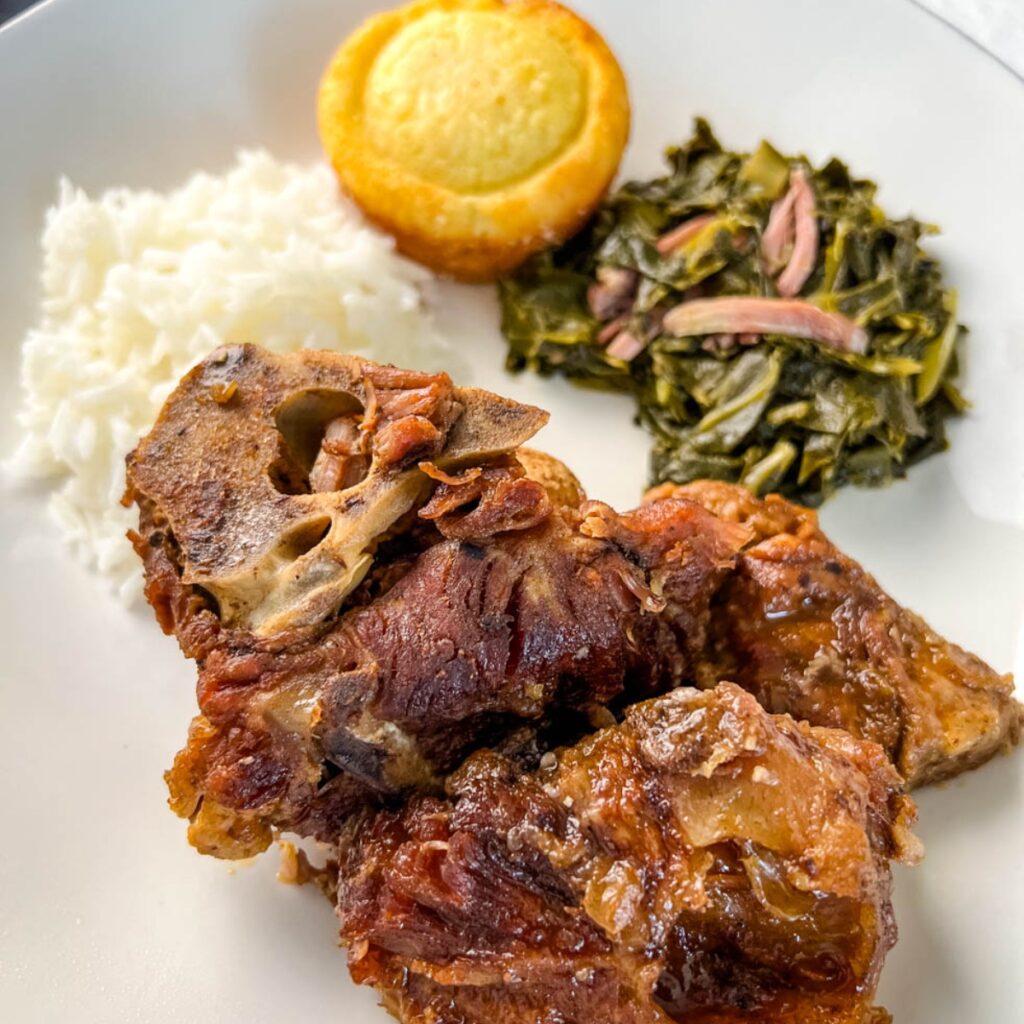 southern pork neck bones on a white plate with rice, collard greens, and cornbread