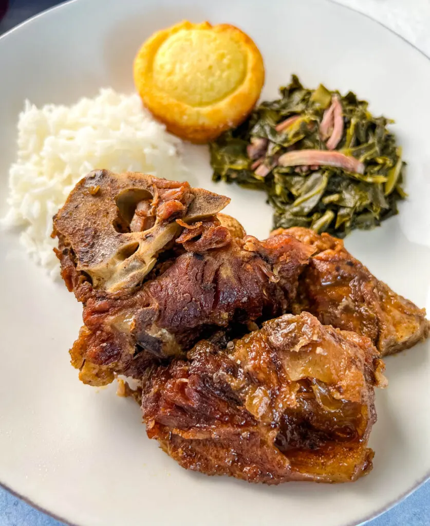 southern pork neck bones on a white plate with rice, collard greens, and cornbread