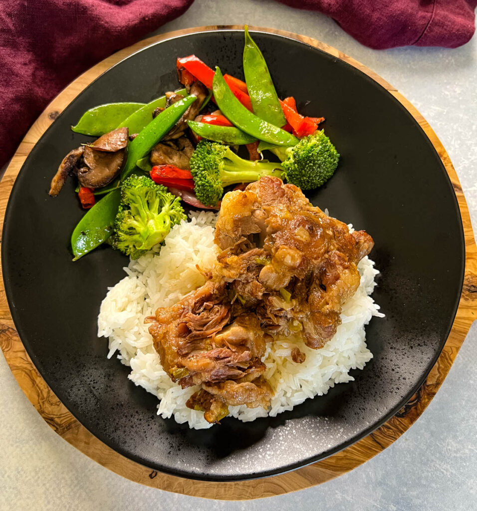 oxtail on a plate with white rice, gravy, and vegetables