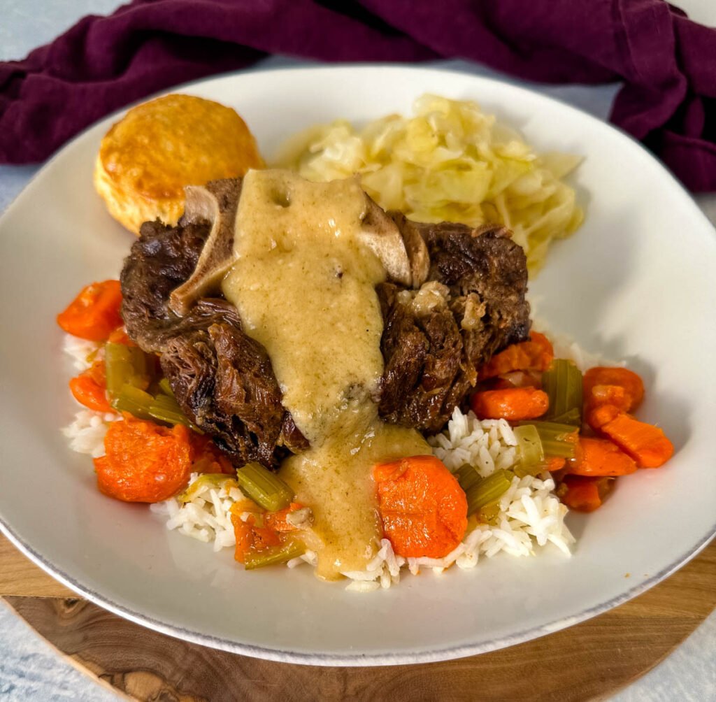 beef neck bones with gravy, cabbage, rice, and carrots on a plate