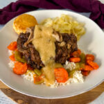 beef neck bones with gravy, cabbage, rice, and carrots on a plate