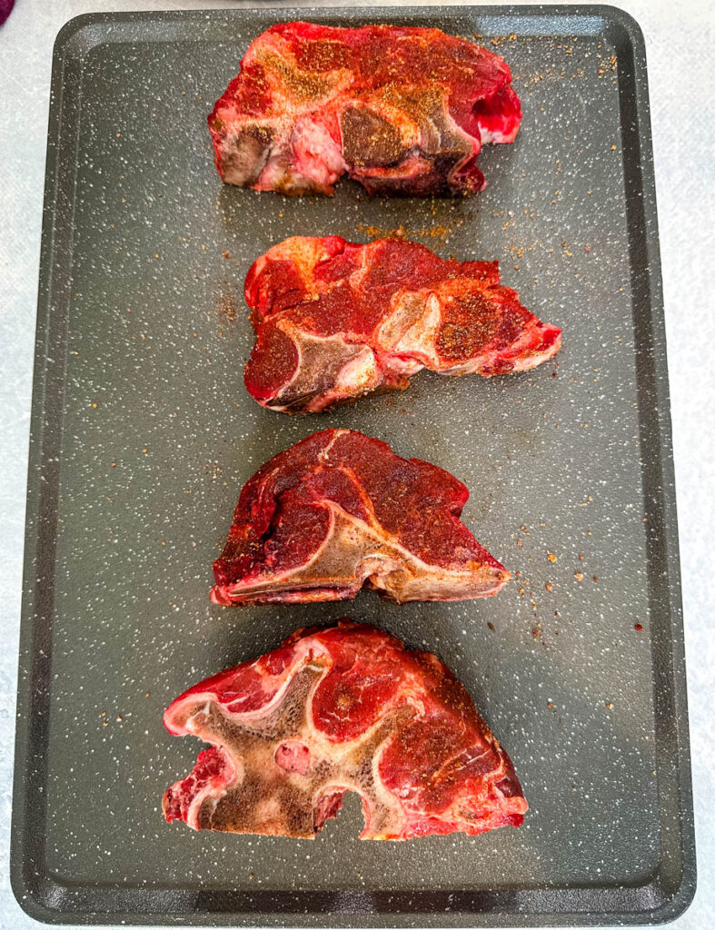 raw seasoned beef neck bones on a sheet pan