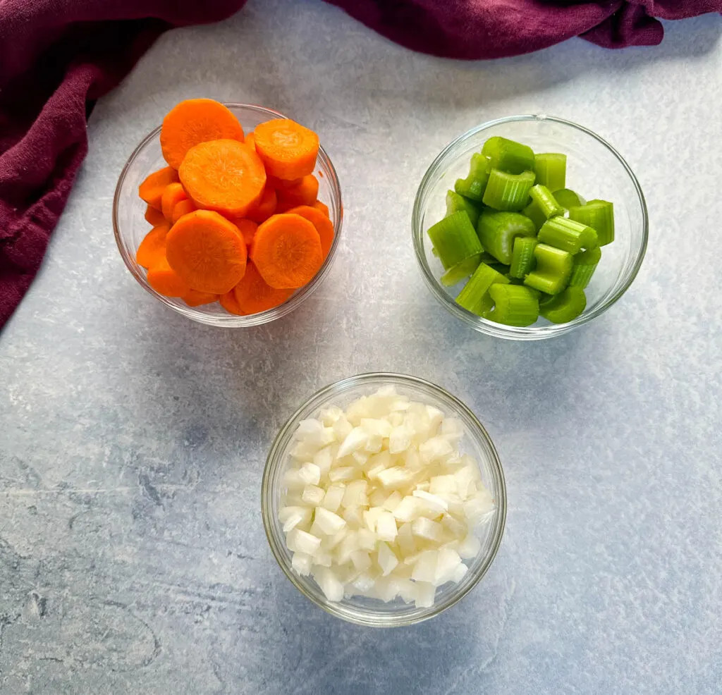 fresh carrots, celery, and onions in separate glass bowls