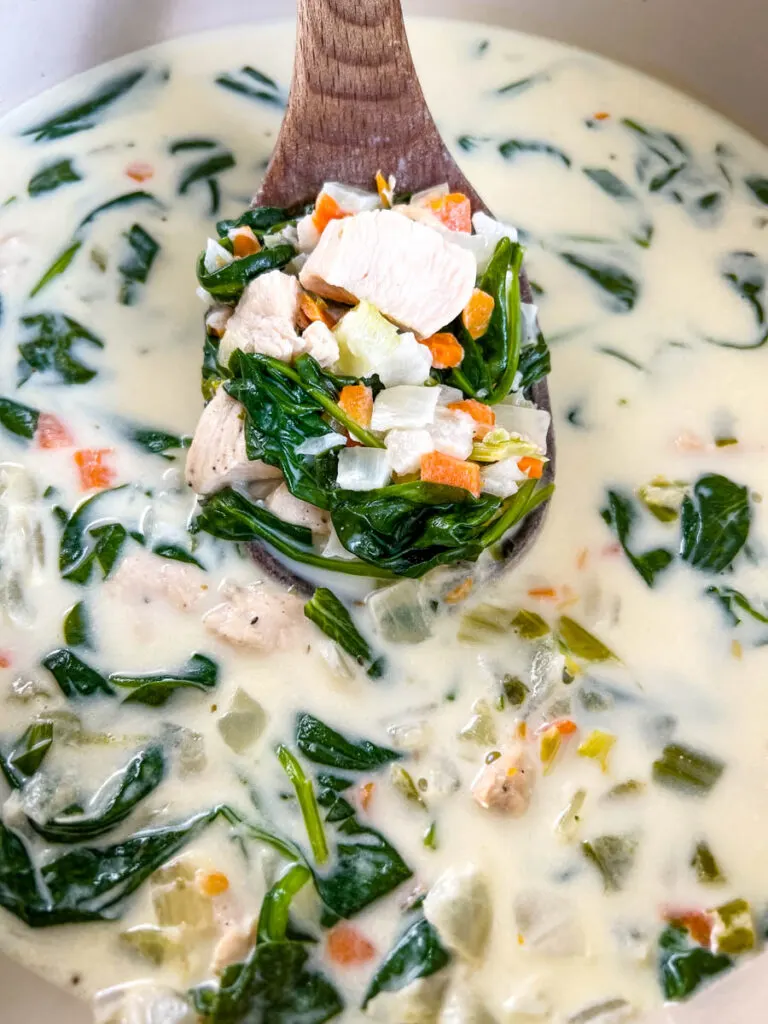 chicken florentine soup and spinach in a soup pot with a wooden spoon