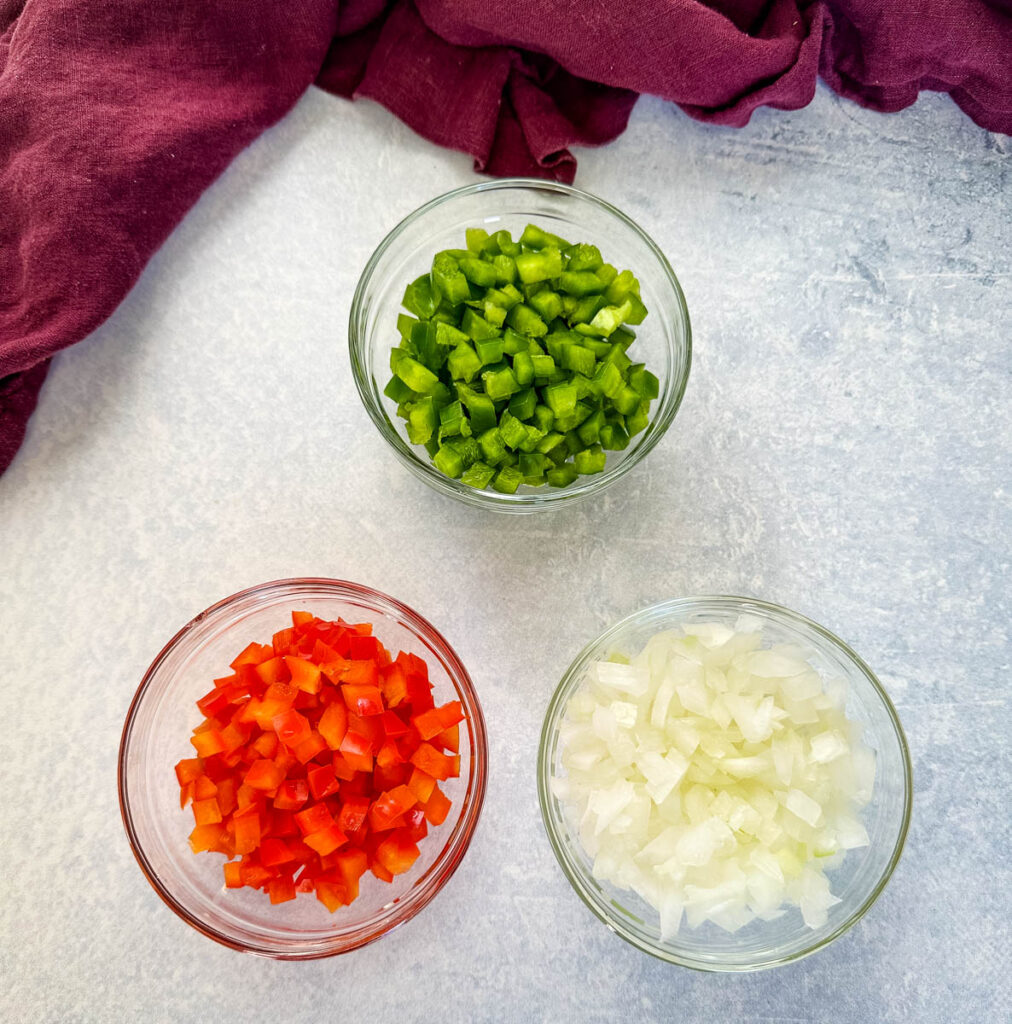 chopped green peppers, red peppers, and onions in separate glass bowls