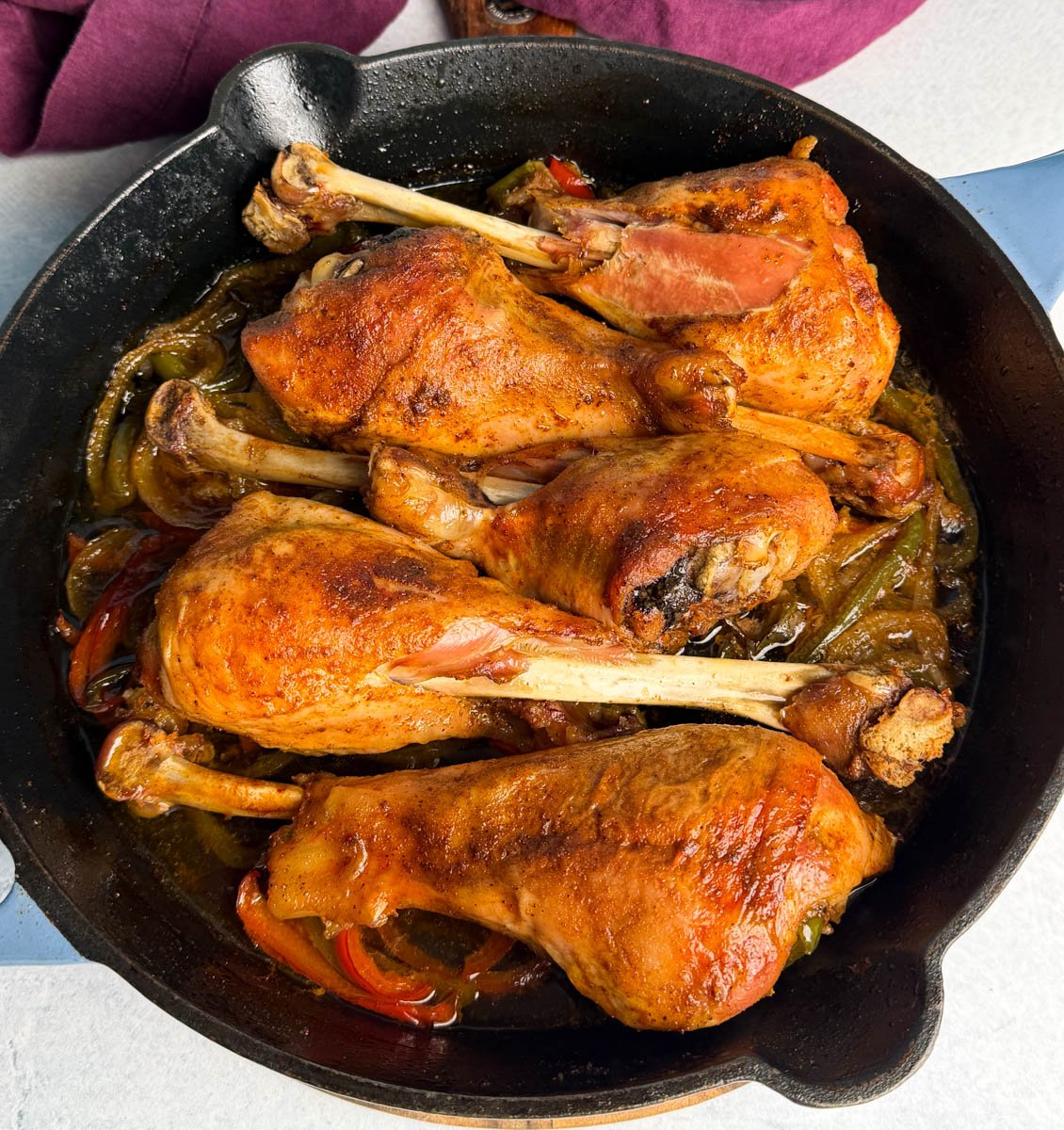 Golden brown baked turkey legs in a cast iron skillet with sautéed onions and bell peppers. The turkey skin looks crisp and caramelized, with rich juices pooling at the bottom of the pan.