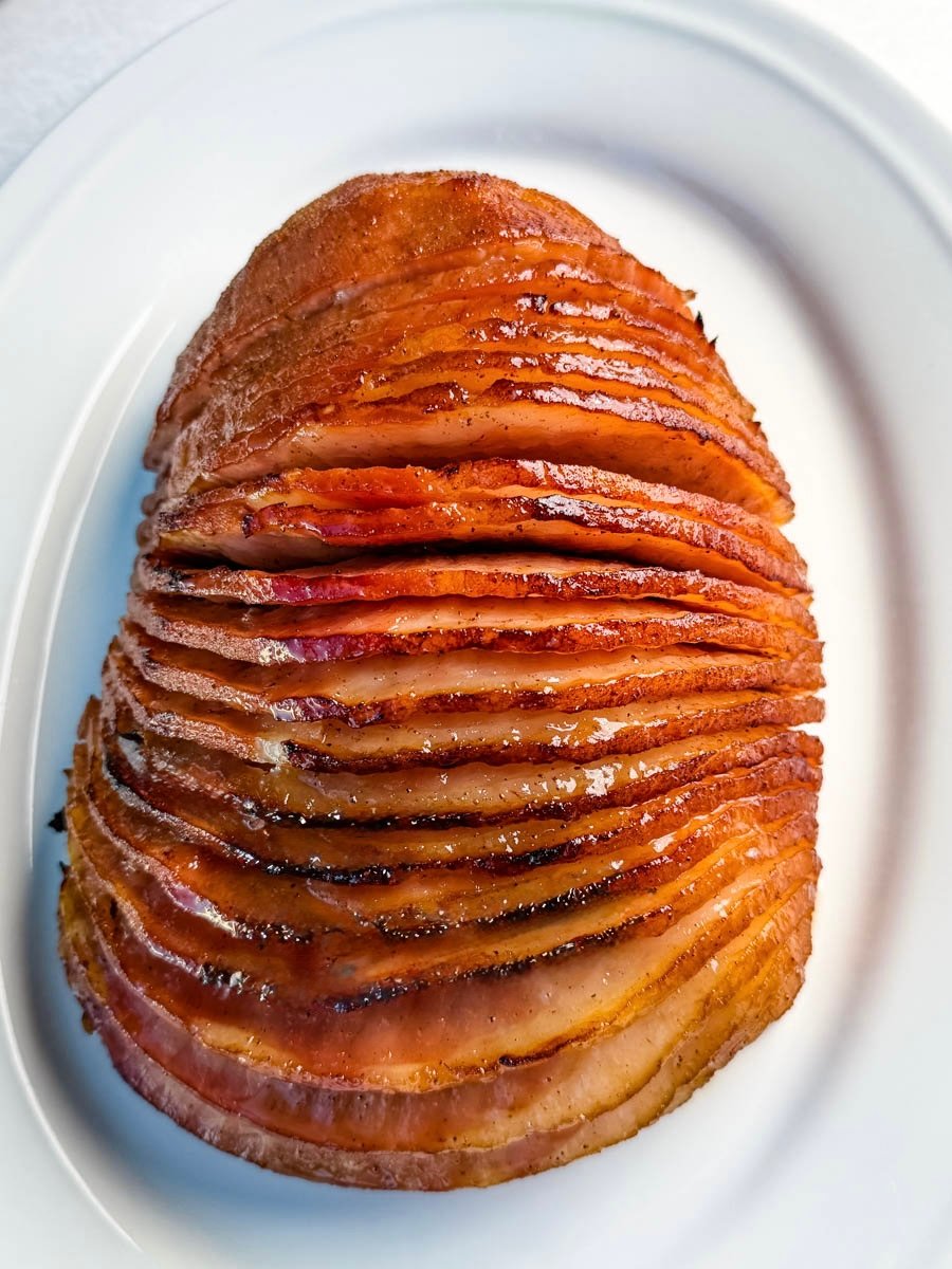 A perfectly cooked, spiral-sliced honey-glazed ham resting on a white serving platter, showing a caramelized, shiny finish.