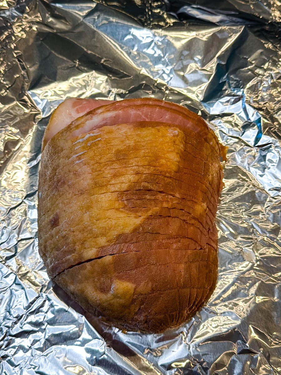 A small, pre-cooked ham resting on a sheet of aluminum foil, ready to be seasoned and cooked.