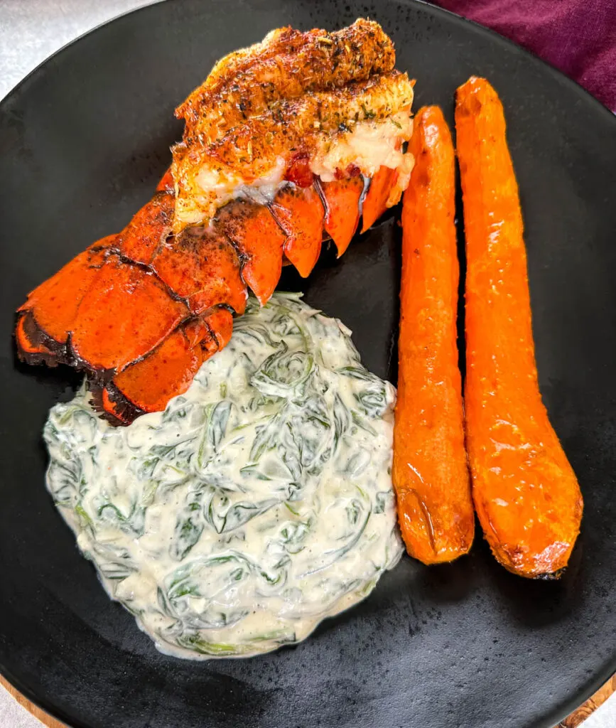 lobster, carrots, and creamed spinach on a black plate