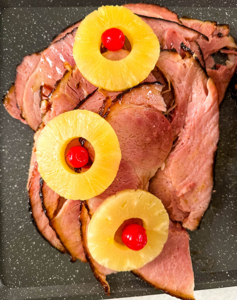 Traeger smoked ham sliced on a plate with pineapples and cherries