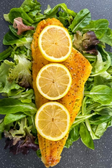 smoked cod fillet with lemons on a pan with greens