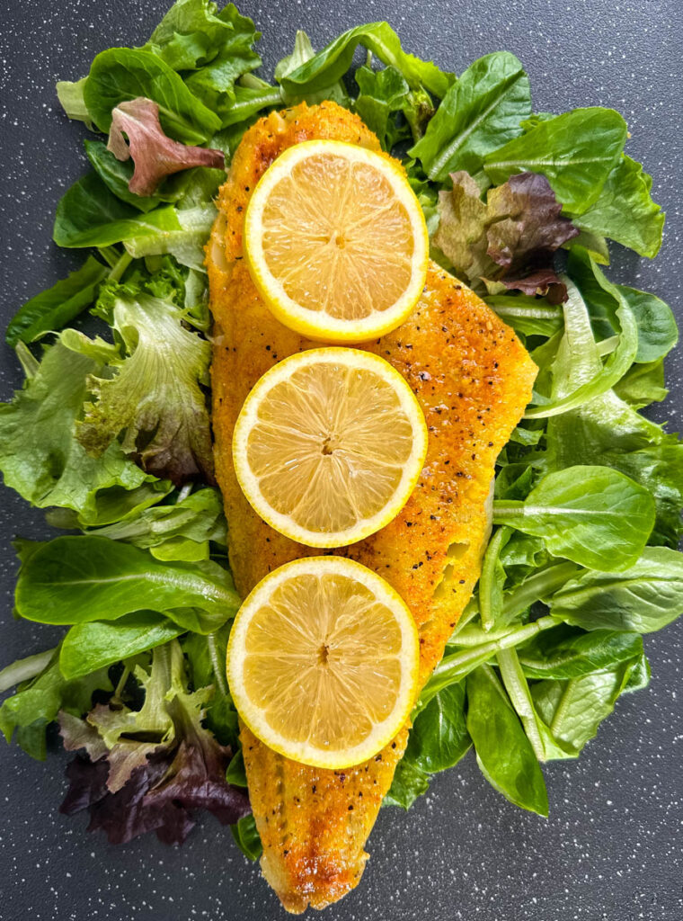 smoked cod fillet with lemons on a pan with greens