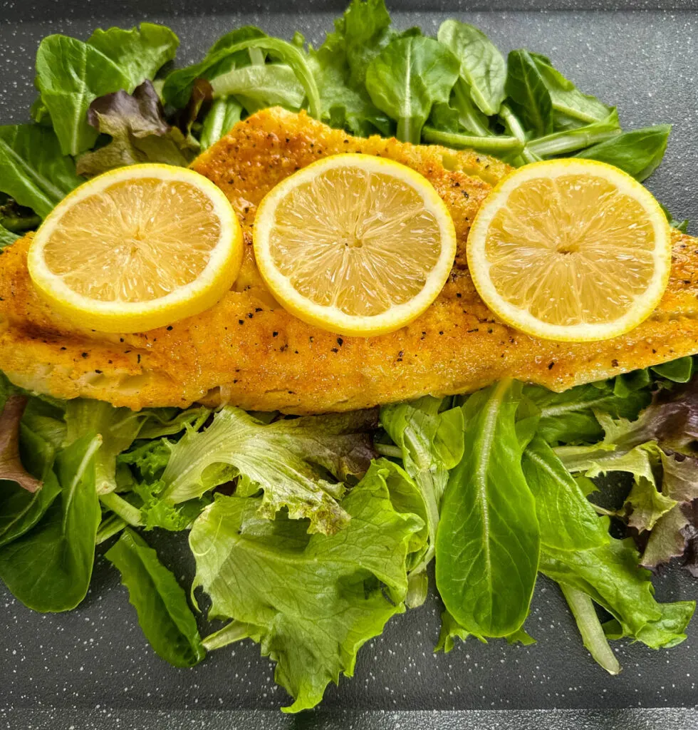 smoked cod fillet with lemons on a pan with greens