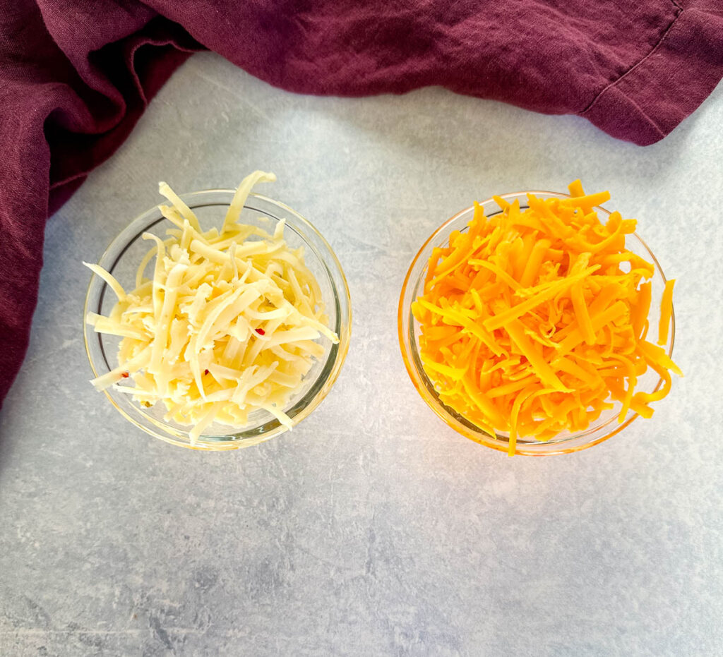 shredded cheddar jack and and cheddar cheese in separate glass bowls
