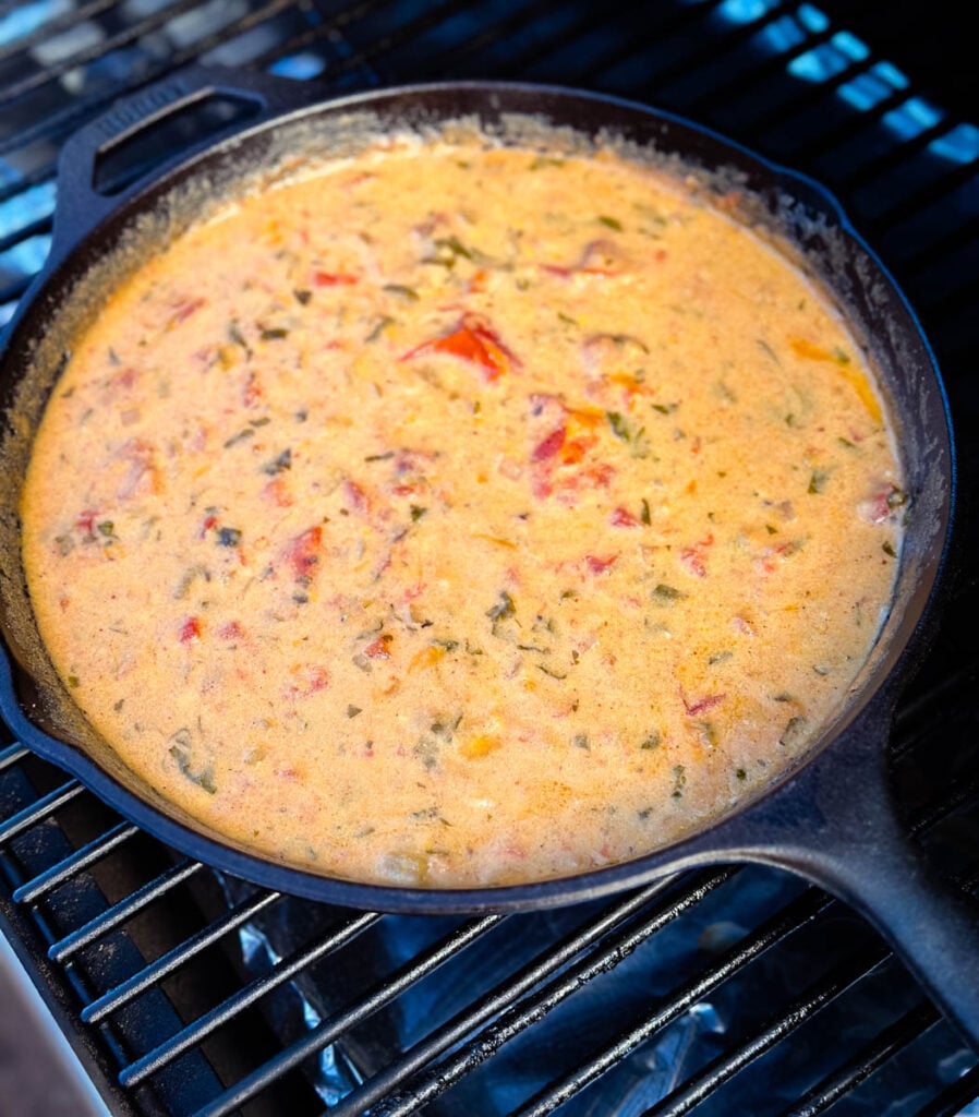 queso cheese dip in a cast iron skillet on a Traeger smoker grill
