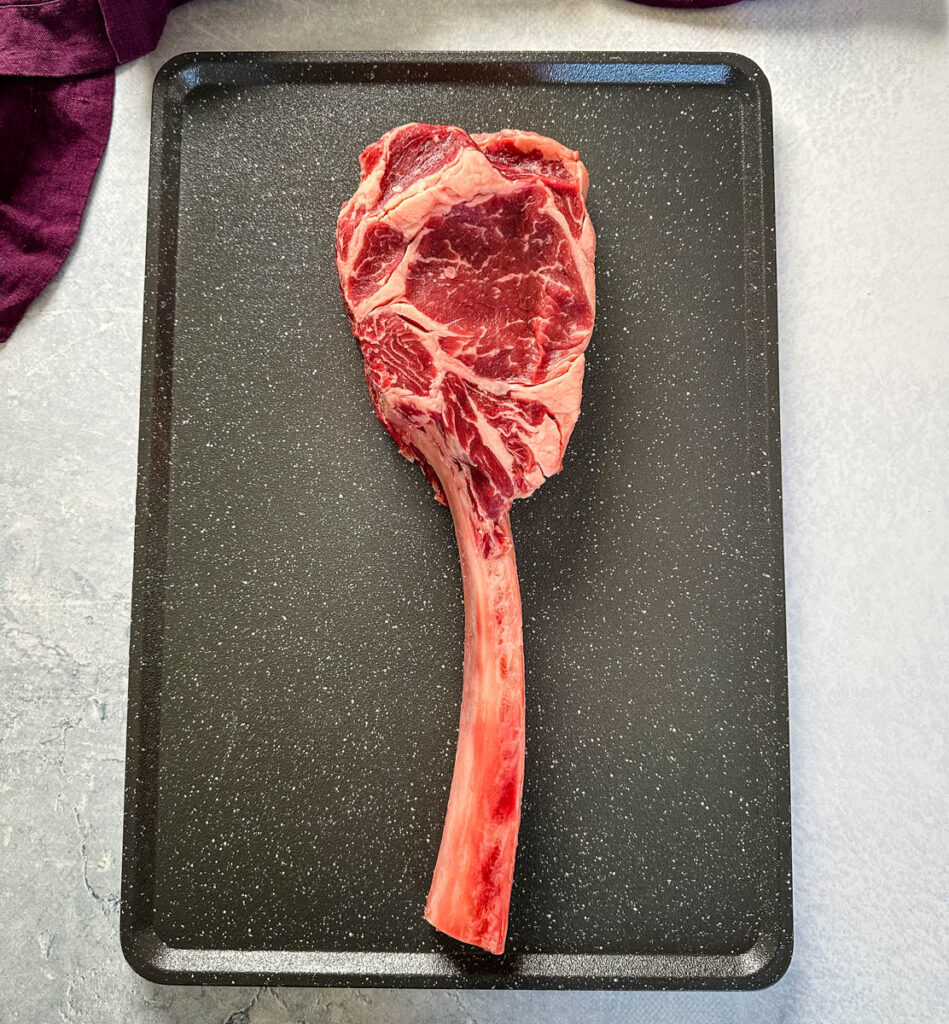 raw tomahawk steak with butter on a platter