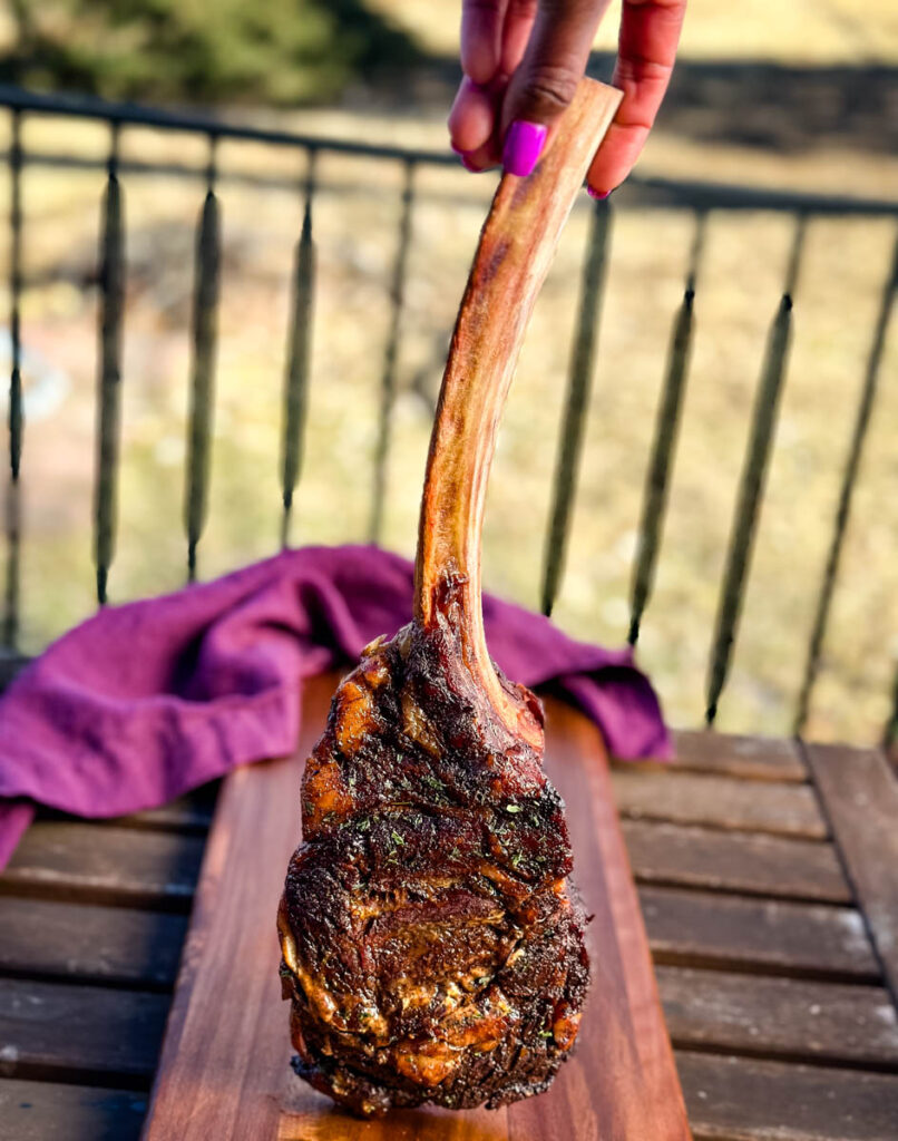 person holding a smoked tomahawk steak by the bone