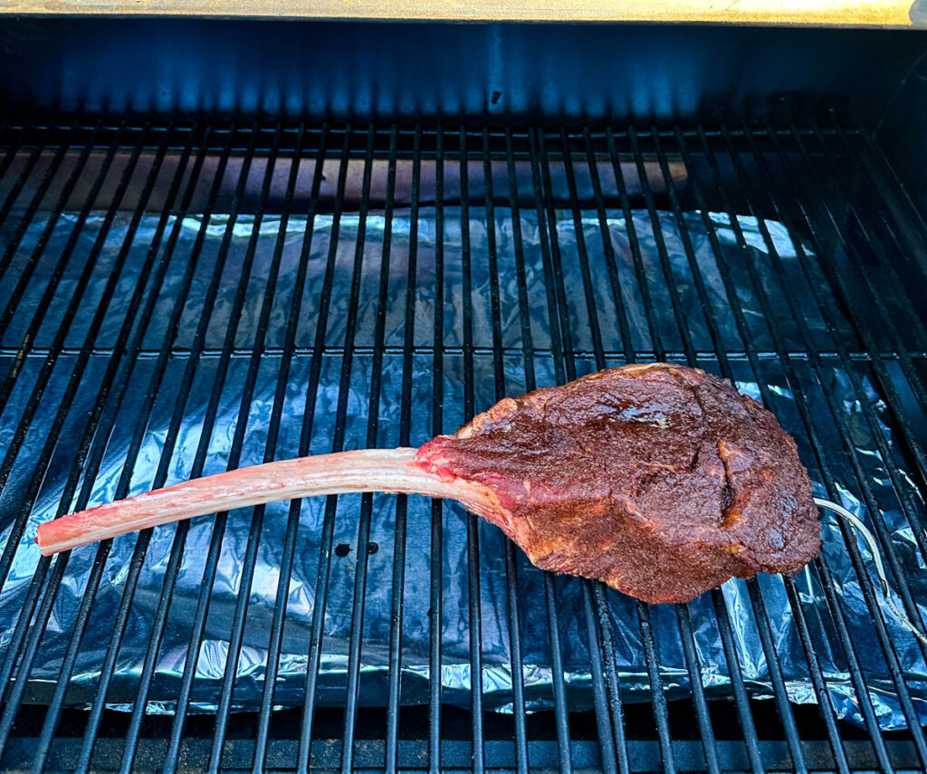 raw seasoned tomahawk steak with butter on a Traeger pellet grill