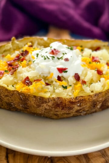 smoked baked potatoes on a plate loaded with sour cream, cheese, and bacon